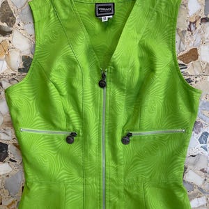 Może przedstawiać: Zielona sukienka bez rękaw&oacute;w z zamkiem błyskawicznym z przodu i wirującym wzorem. Sukienka ma dekolt w kształcie litery V i metkę z napisem "VERSACE" z przodu.