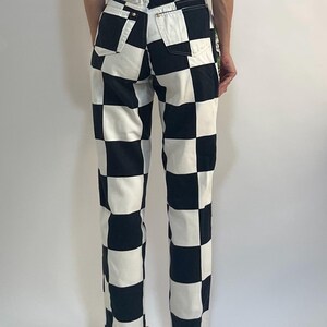 May include: High-waisted denim pants featuring a bold black and white checkered pattern. These trousers include a classic five-pocket design with visible belt loops, a button closure at the waist, and a straight-leg cut that reaches the ankles.