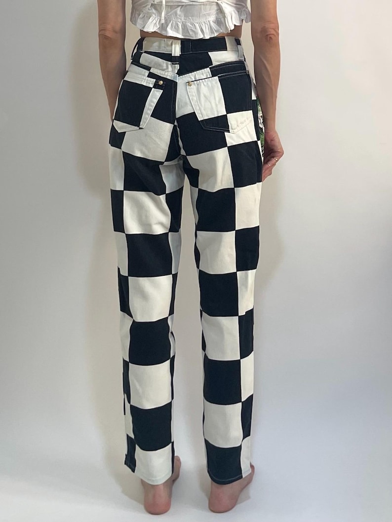 May include: High-waisted denim pants featuring a bold black and white checkered pattern. These trousers include a classic five-pocket design with visible belt loops, a button closure at the waist, and a straight-leg cut that reaches the ankles.