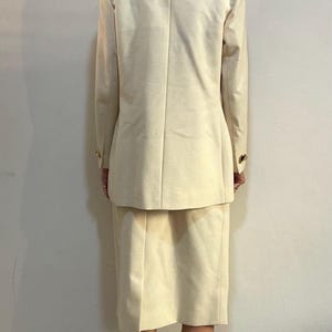 Puede incluir: Traje de falda color crema con tejido acanalado texturizado. El traje incluye una blazer con botones dorados y una falda a juego hasta la rodilla. Un estilo cl&aacute;sico y profesional.