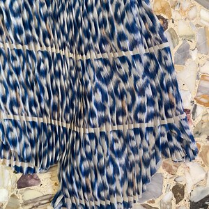 Op de afbeelding: Geplooide stof met een blauw-witte dierenprint. De stof is in verticale plooien gevouwen, waardoor een textuur ontstaat. Het patroon is een mix van blauw en wit, met een luipaardachtig ontwerp.