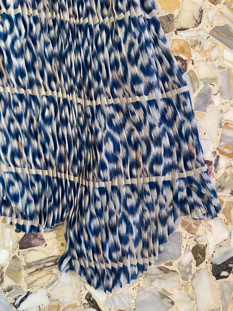 Op de afbeelding: Geplooide stof met een blauw-witte dierenprint. De stof is in verticale plooien gevouwen, waardoor een textuur ontstaat. Het patroon is een mix van blauw en wit, met een luipaardachtig ontwerp.