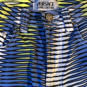 Puede incluir: Vaqueros a rayas azules, amarillas y blancas con una etiqueta negra de Versace Jeans Couture.