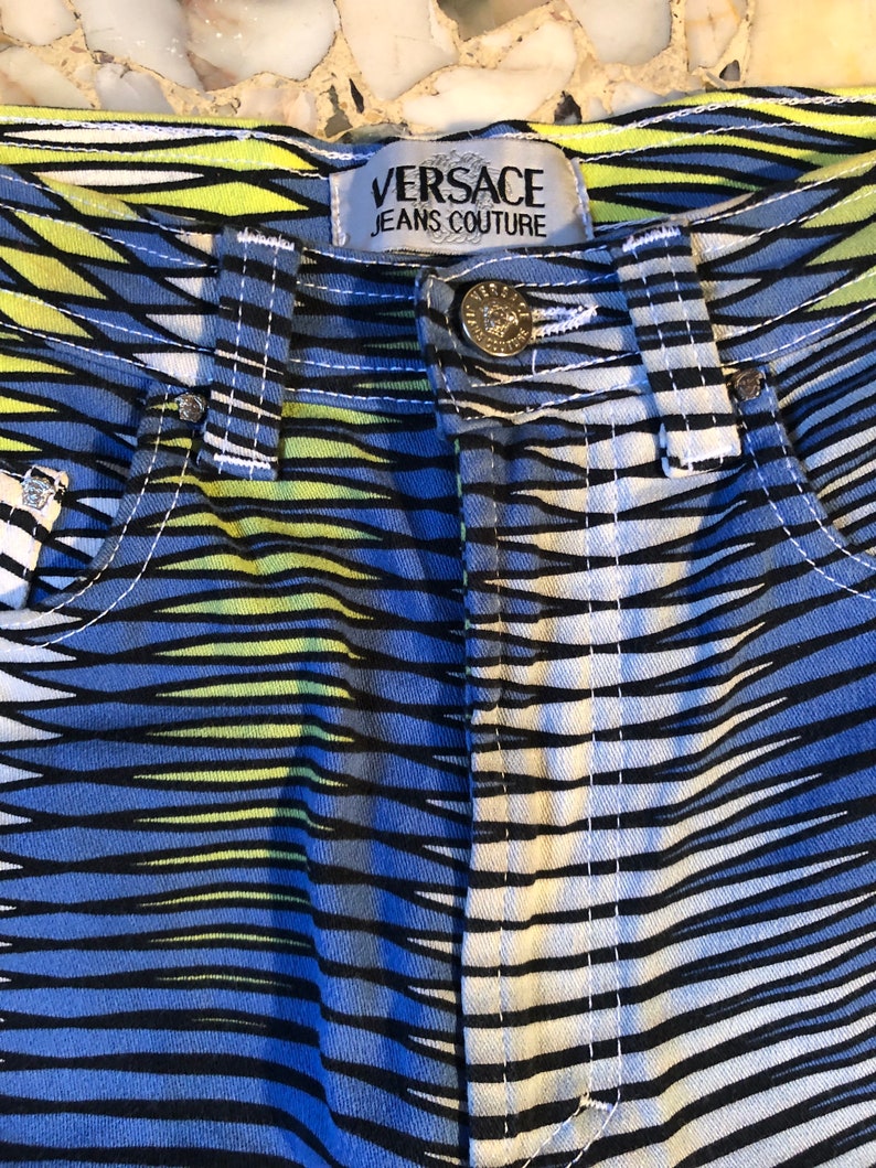 Puede incluir: Vaqueros a rayas azules, amarillas y blancas con una etiqueta negra de Versace Jeans Couture.