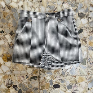 May include: Black and white checkered shorts with decorative silver-toned buttons and zippers. The shorts have a high waist and a small label that reads "VERSACE".