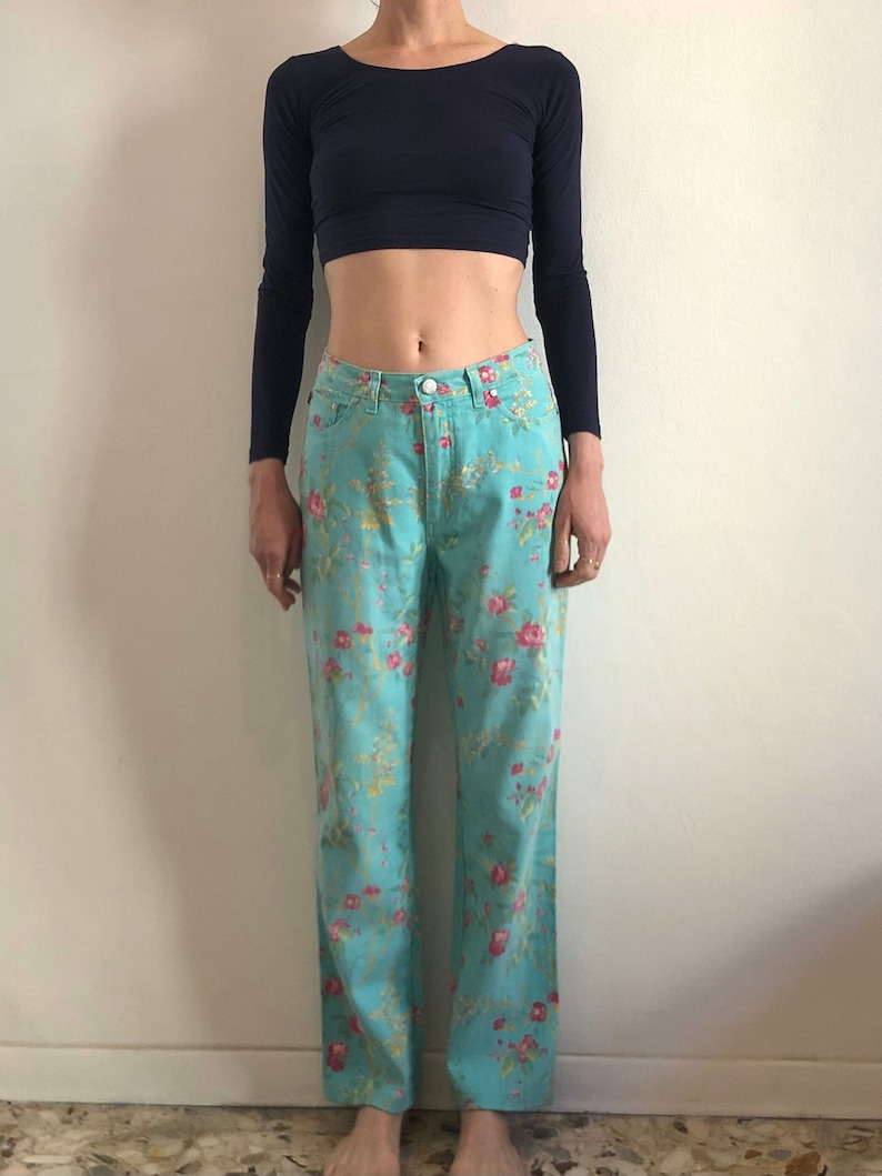 May include: A pair of light blue jeans with a floral print. The jeans have a straight leg and a mid-rise waist.