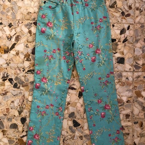 May include: A pair of light blue jeans with a floral print featuring pink and red roses. The jeans have a straight leg and a classic five-pocket design.