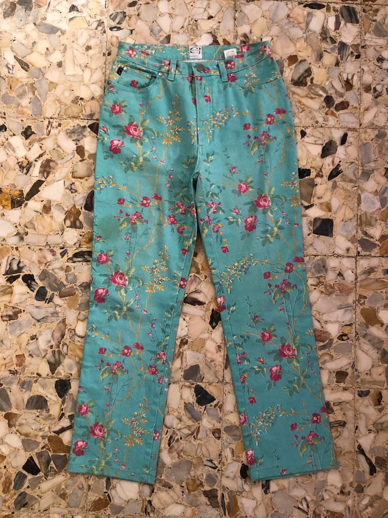 May include: A pair of light blue jeans with a floral print featuring pink and red roses. The jeans have a straight leg and a classic five-pocket design.