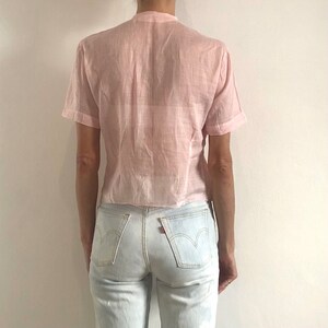 Pu&ograve; includere: Una camicia a maniche corte di colore rosa pallido, trasparente, con bottoni e vestibilit&agrave; rilassata. La camicia &egrave; realizzata in un tessuto leggero e ha un orlo leggermente corto.