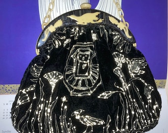 May include: Black velvet handbag with a cream-colored clasp and chain. The bag features an embroidered design with birds and floral elements. The clasp is adorned with bird-shaped accents, adding a vintage touch to this elegant accessory.