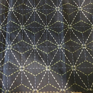 May include: Black fabric with a geometric pattern of white and yellow stitching. The pattern is made up of repeating stars and diamonds.