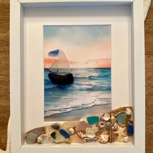 May include: A framed watercolor painting of a sailboat on the ocean at sunset, with a beach scene below the painting made of seashells and sea glass.