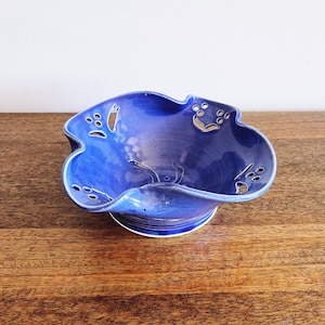 May include: A blue ceramic bowl with a scalloped edge and decorative cutouts. The bowl is handmade and has a unique, rustic look.