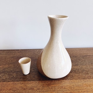 May include: A white ceramic sake set with a brown glaze. The set includes a larger bottle and a smaller cup.