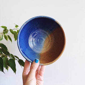 May include: A blue and brown ceramic bowl with a glazed finish. The bowl has a slight swirl pattern in the blue glaze.