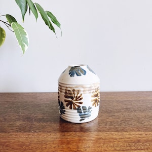 May include: A white ceramic vase with a brown and blue floral pattern. The vase has a rounded body and a slightly flared opening.
