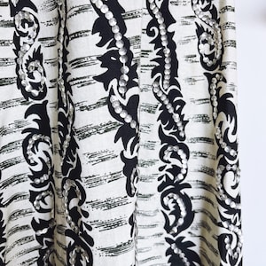 May include: Close-up of a fabric with a black and white pattern. The fabric features vertical stripes with a black floral design and silver sequins. The background has a white base with horizontal black brushstrokes.