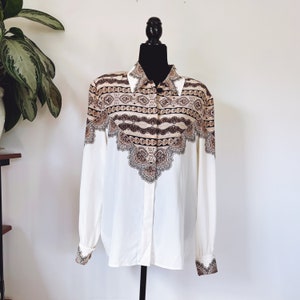 May include: A white long-sleeve button-up shirt with a brown and beige paisley print. The print features a geometric pattern with chains and paisley shapes.
