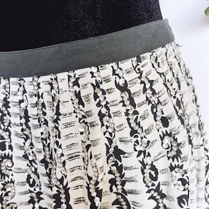 May include: A black and white patterned skirt with silver sequins. The skirt has a black waistband and a flowing design. The fabric features a repeating pattern of black shapes and white stripes, with vertical lines of sequins.