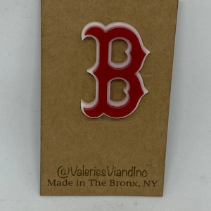 May include: A red and white acrylic letter B pin attached to a rectangular brown cardboard backing. The backing features the text @ValeriesViandInc and Made in The Bronx, NY printed in black ink at the bottom of the display card.