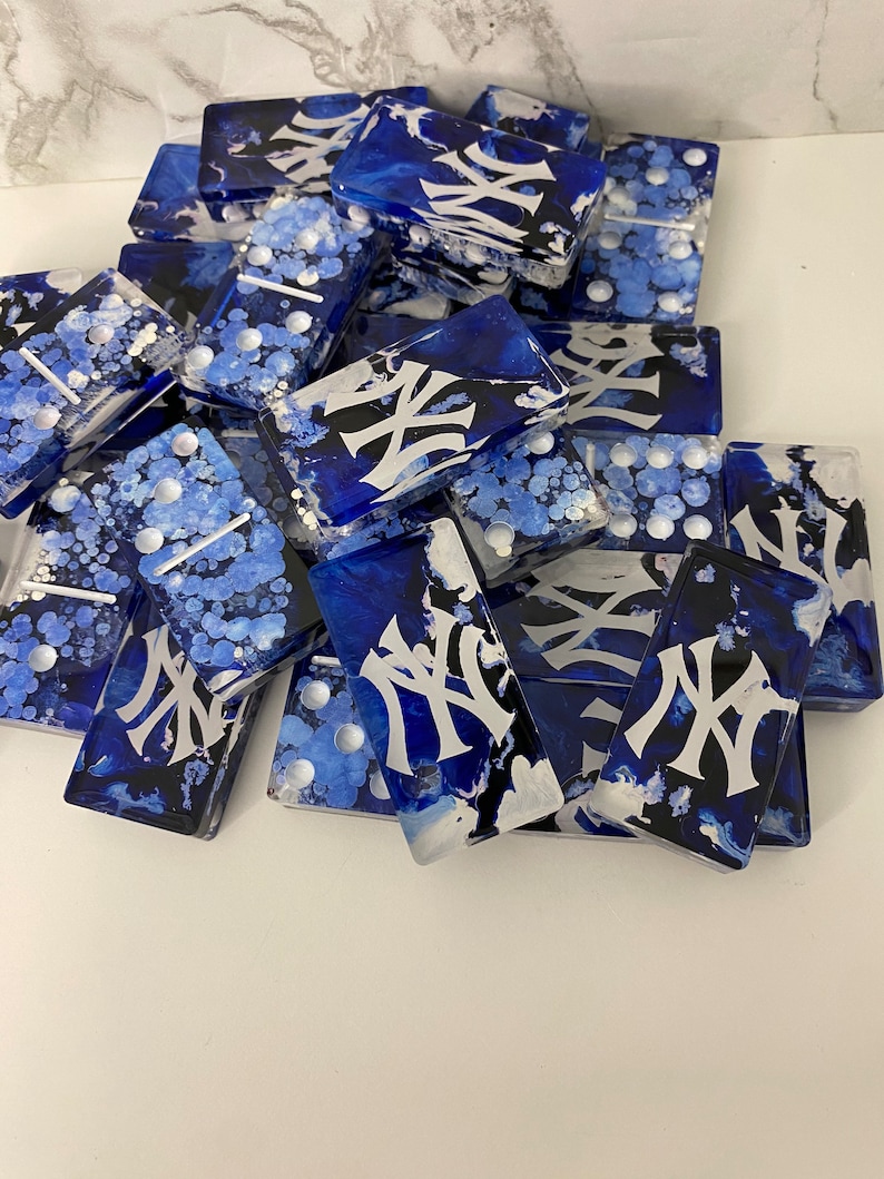 May include: A set of blue and white dominoes with a black and white "NY" logo on each tile. The dominoes are hand-painted with a unique marbled effect.