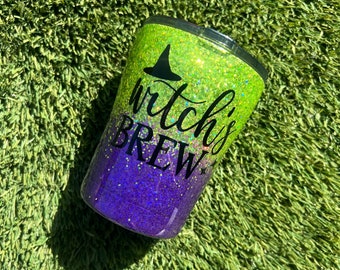 May include: A green and purple glitter tumbler with a black witch's hat and the text "witch's brew".
