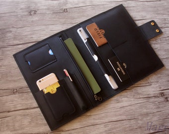 May include: Black leather travel wallet with multiple pockets and slots for carrying cards, cash, a passport, and a phone. The wallet is open and laid flat on a wooden surface.