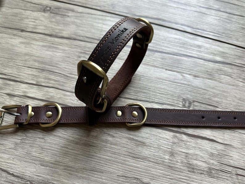 May include: Two brown leather dog collars with brass hardware. The larger collar has the name "Bruce Monika" engraved on it.