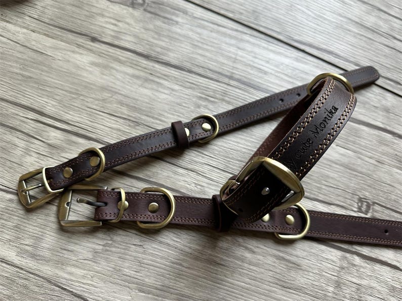 May include: Two brown leather dog collars with brass hardware. The larger collar has the name "Grace Monika" engraved on it.