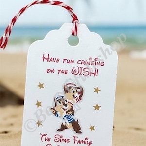May include: White gift tag with red text that says "Have fun cruising on the Wish!" with a cartoon image of Chip and Dale dressed as sailors. The tag also has gold stars and the text "The Sims Family Cabin 7574".