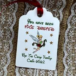 May include: White gift tag with green and red text that reads "You have been pixie dusted" with a cartoon image of Tinkerbell. The tag also includes the text "By: The Coop Family Cabin 6562".