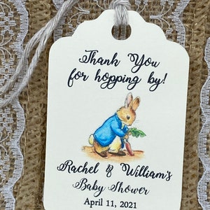 May include: White thank you tag with a blue and brown illustration of Peter Rabbit holding a carrot. The tag says "Thank You for hopping by! Rachel & William's Baby Shower April 11, 2021".
