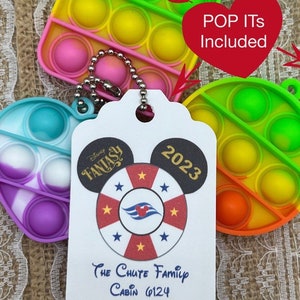 May include: A white tag with a Mickey Mouse head design, featuring the text "Disney Fantasy 2023" and a red, white, and blue nautical wheel with stars. The tag also includes the text "The Chute Family Cabin 6124". The tag is attached to a colorful pop-it toy keychain.