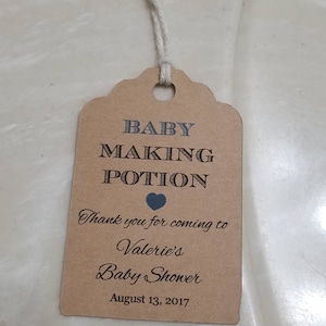 May include: A brown paper tag with the text "BABY MAKING POTION" and "Thank you for coming to Valerie's Baby Shower August 13, 2017". The tag has a heart symbol and a string attached for hanging. The tag is for a baby shower.