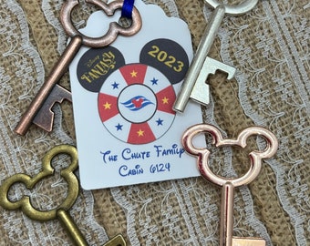 May include: Four Mickey Mouse shaped key bottle openers in different colors: silver, copper, gold, and rose gold. The key openers are hanging from a blue ribbon and a white tag with the text "Disney Fantasy 2023 The Chute Family Cabin 6124".