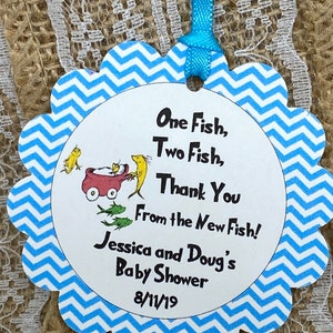 May include: A blue and white chevron patterned baby shower favor tag with the text "One Fish, Two Fish, Thank You From the New Fish! Jessica and Doug's Baby Shower 8/11/19"
