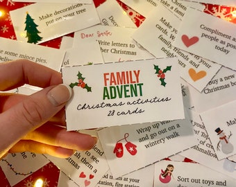 May include: A collection of white cards with Christmas-themed activities, including a card that reads "Family Advent Christmas activities 28 cards." The cards are scattered on a red surface with snowflake patterns and fairy lights.