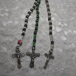 May include: Three silver cross charms with beaded chains. The chains are white, green, and clear.