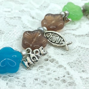 May include: A charm bracelet with blue, green, and brown glass beads. The charms are silver and say "Hope" and "Jesus".