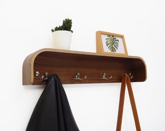 May include: A wooden wall-mounted shelf with a curved front edge and three hooks. A black leather jacket hangs on one hook, and a brown leather strap hangs on another. A small potted plant sits on the shelf.