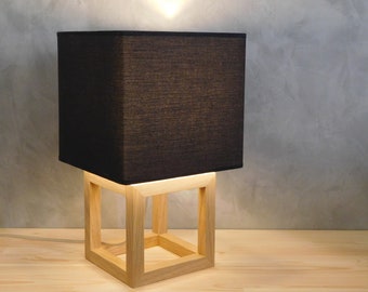 May include: A black fabric lampshade with a wooden square base. The lampshade is lit and the light shines through the fabric.