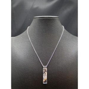 May include: Silver-toned necklace with a rectangular pendant. The pendant features a dragonfly design in black and silver, with colorful accents. The necklace is displayed on a black mannequin.