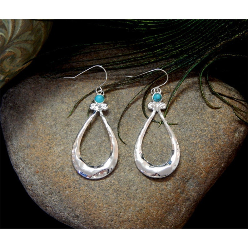 K&ouml;nnte beinhalten: Silberne Ohrringe mit einem t&uuml;rkisfarbenen Steinakzent. Die Ohrringe sind tropfenf&ouml;rmig mit einem Ausschnitt in der Mitte.