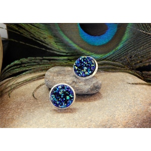 May include: A pair of silver stud earrings with blue and green iridescent glitter. The earrings are round and have a flat back.