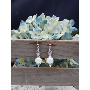 May include: A pair of silver dangle earrings with white round beads and ornate silver accents.