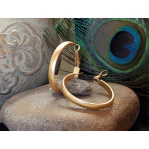 May include: A pair of gold hoop earrings with a brushed finish. The earrings are large and have a simple, elegant design.