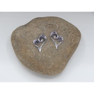 Puede incluir: Un par de pendientes de plata en forma de coraz&oacute;n con un dise&ntilde;o de espiral. Los pendientes cuelgan de una roca.