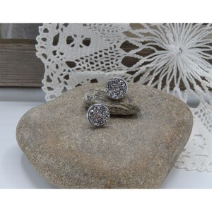 May include: A pair of silver stud earrings with a round, sparkly, silver glitter design.