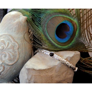 May include: A silver bangle bracelet with a black gemstone set in a floral design.