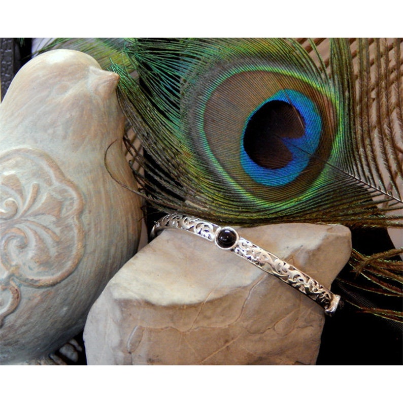 May include: A silver bangle bracelet with a black gemstone set in a floral design.